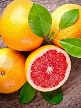 Citrus 'Star Ruby' Grapefruit 4L Pot grapefruits with green leaves lie on a wooden surface, one sliced to show its bright red center.