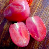 Two halved Tomato 'Mamma Mia' alongside a whole one on a wooden surface evoke the simple joys of an Italian cooking session.