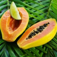A Paw Paw 'Fijian' papaya, halved with seeds and adorned by a lime wedge, rests gracefully on green palm leaves.
