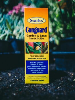 A box of Searles Conguard Garden & Lawn Insecticide 500ml, in front of a plant.