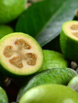 Fresh feijoas (pineapple guavas) with one cut in half, revealing the flesh and seeds, on a wooden surface. feijoa acca