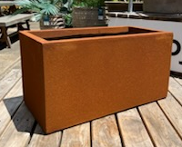 A rectangular corten steel Brighton Trough Rust L planter box, 100x46x46cm, on a wooden deck.