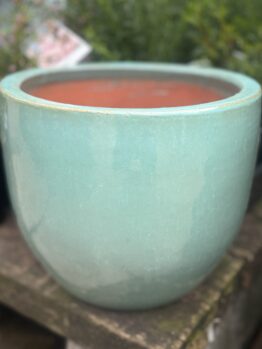 A Glazed Cylinder Moss Green S 20x20cm pot sits on a stone surface, with blurred green foliage in the background.