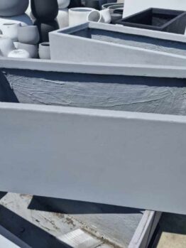 The sunlit outdoor surface features multiple rectangular gray concrete planters, such as the GardenLite Trough Cement M model with dimensions of 80x37x37cm.