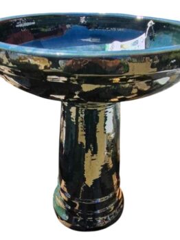 The Sorrento Birdbath features a tall glazed ceramic design with a deep blue basin and column pedestal, adorned in an iridami pattern of mottled green and brown hues. Size: 46x60cm.