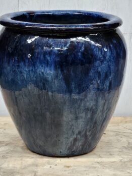 A large, glossy, dark blue ceramic vase with a rounded shape and wide rim, standing on a wooden surface.