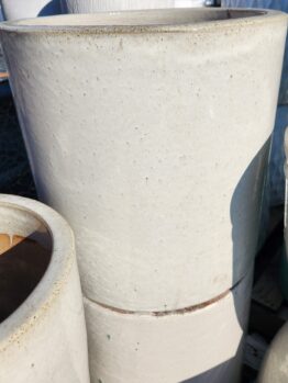 Two large, stacked, off-white ceramic pots with a smooth, slightly speckled surface, shown outdoors in sunlight.