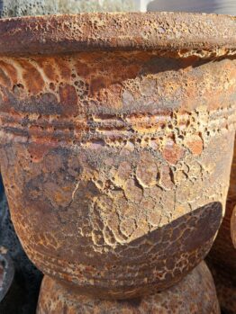 A close-up of a large, weathered terracotta planter with a rough, textured surface and decorative horizontal ridges.