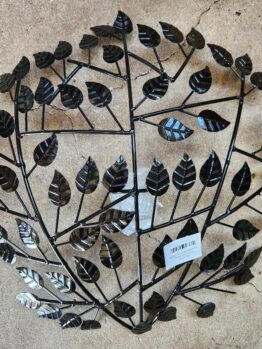 The Raja TeaLight Wall Art Black 46x10cm is a round metal wall decor with a symmetrical tree branch pattern and black leaves, displayed on a concrete surface. A white barcode sticker is near the bottom center.