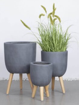 Three GardenLite Egg Planter with Legs Brushed Concrete (SET OF 3) are arranged together; one holds tall green grass, and two are empty.