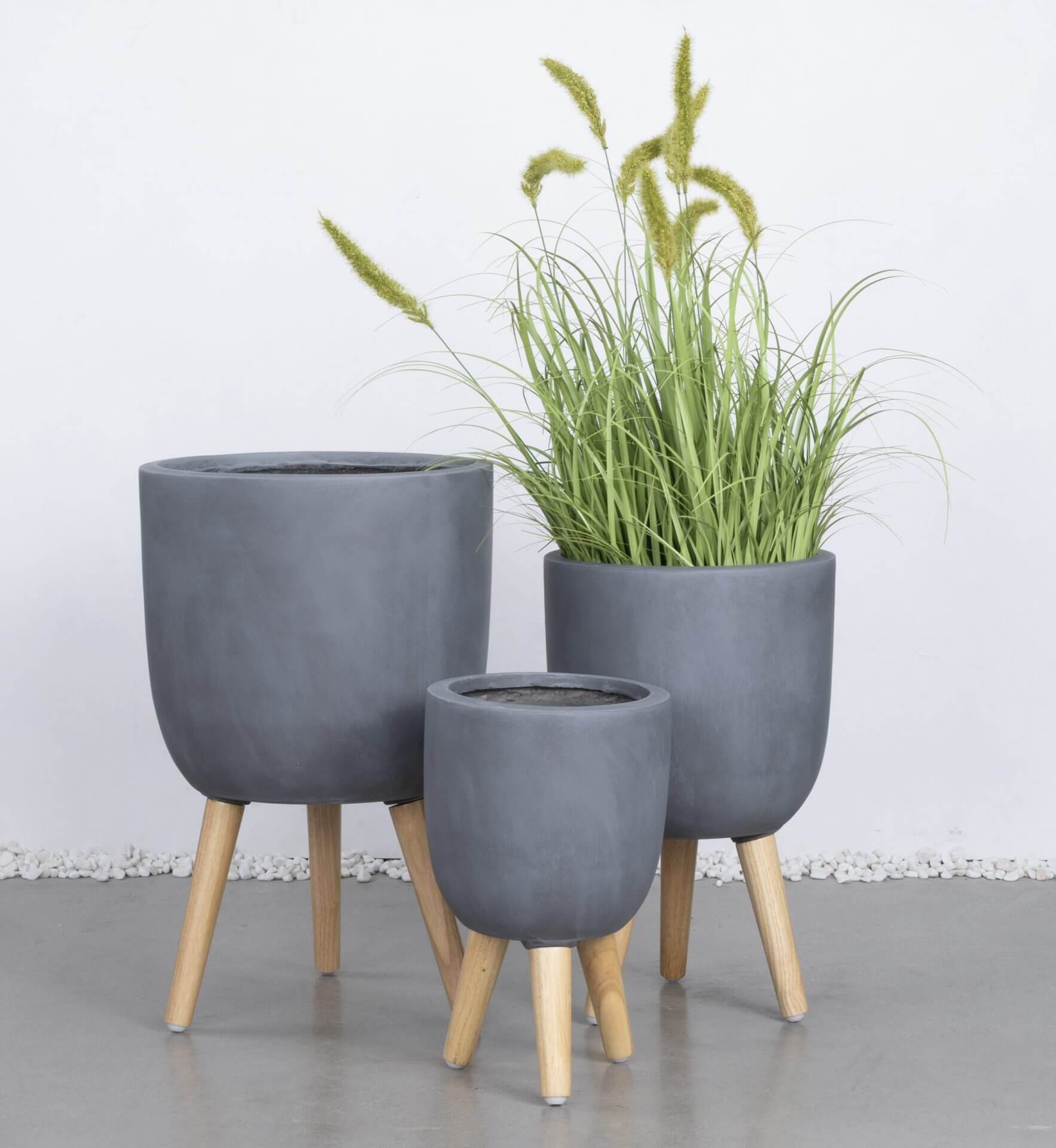 Three GardenLite Egg Planter with Legs Brushed Concrete (SET OF 3) are arranged together; one holds tall green grass, and two are empty.