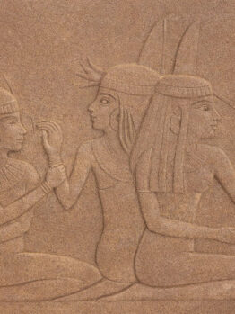 Stone relief depicting three seated ancient Egyptian women, each wearing traditional headdresses and garments, with one woman gesturing and the others engaged in conversation.