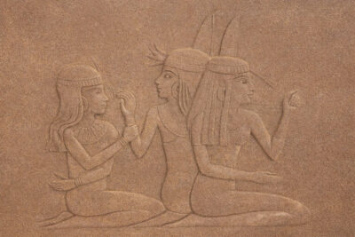 Stone relief depicting three seated ancient Egyptian women, each wearing traditional headdresses and garments, with one woman gesturing and the others engaged in conversation.