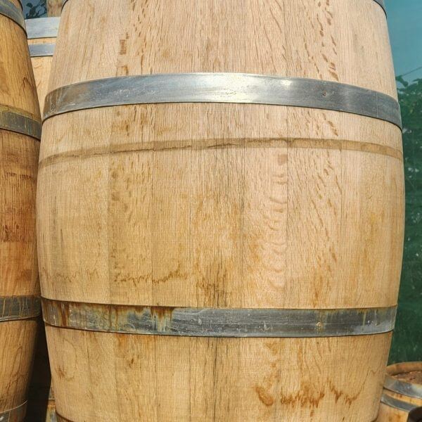 A Wine Barrel (Whole) with metal bands is standing upright on a wooden pallet outdoors.