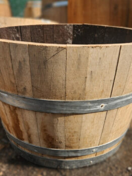 A Wine Barrel (Half) with metal bands and open ends sits on a dirt surface.