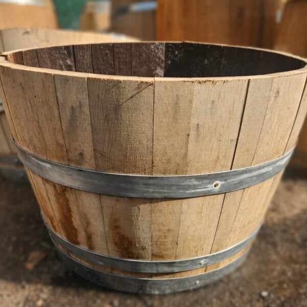 A Wine Barrel (Half) with metal bands and open ends sits on a dirt surface.